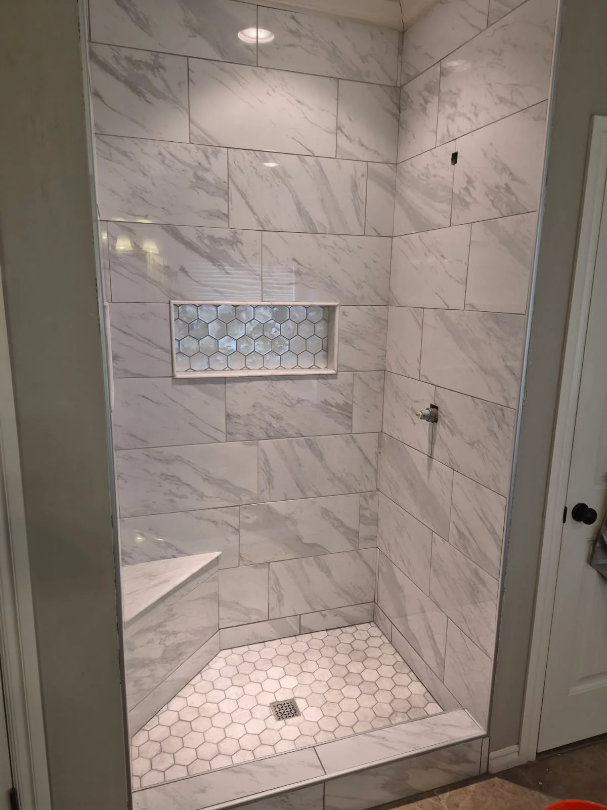 Modern marble tile shower with subway pattern walls, hexagonal floor tiles, and built-in bench