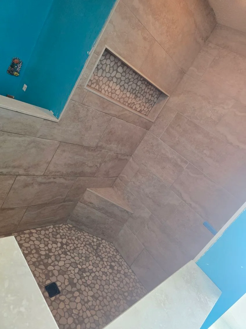 Newly tiled bathroom shower with gray ceramic walls and pebble stone floor