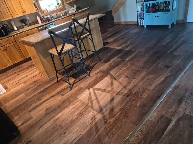 Dark luxury vinyl plank flooring in kitchen with wood cabinets and black bar stools