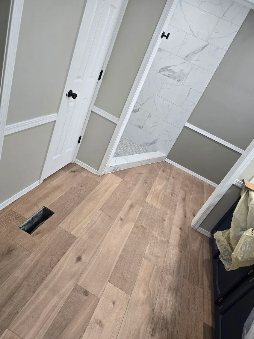Newly installed wood-tone vinyl plank flooring in bathroom with white trim and marble tile shower area