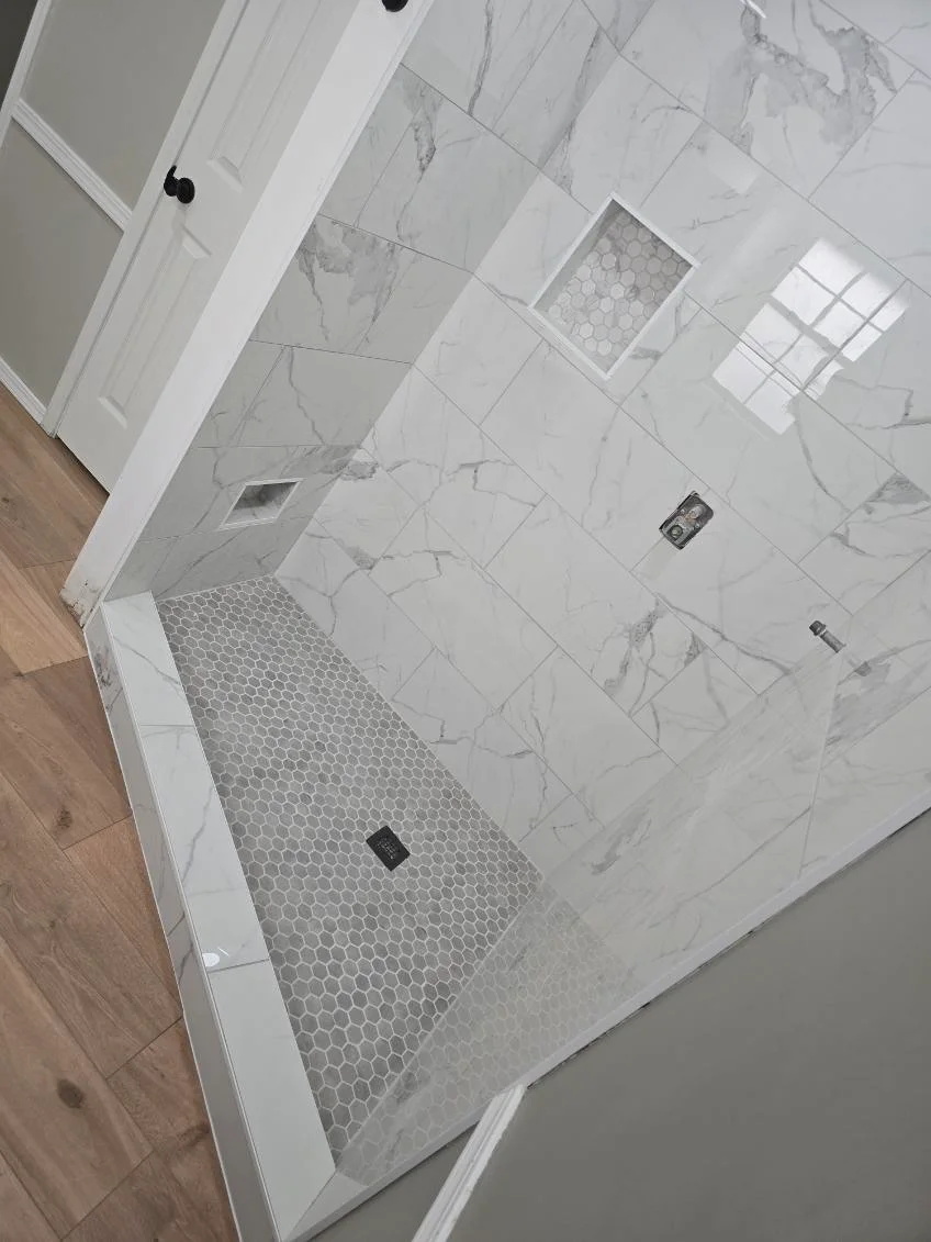 Overhead view of marble tile shower with hexagon mosaic floor and white trim