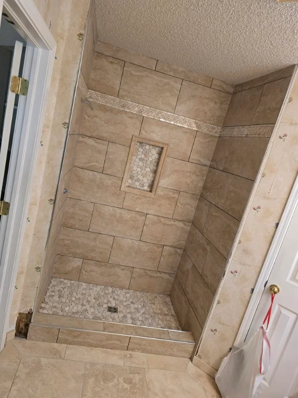 Newly tiled shower with beige ceramic tiles, recessed niche, and pebble floor