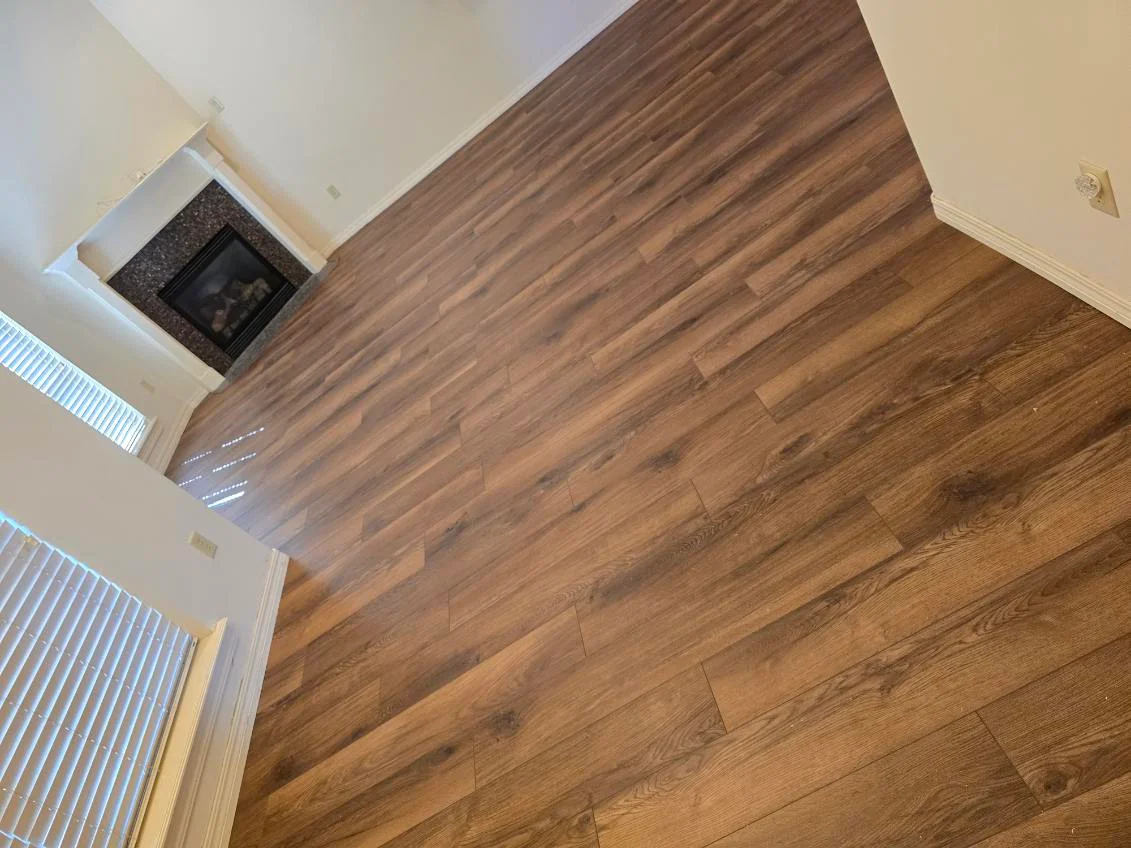 Newly installed engineered hardwood flooring in medium brown tone with fireplace and white trim visible