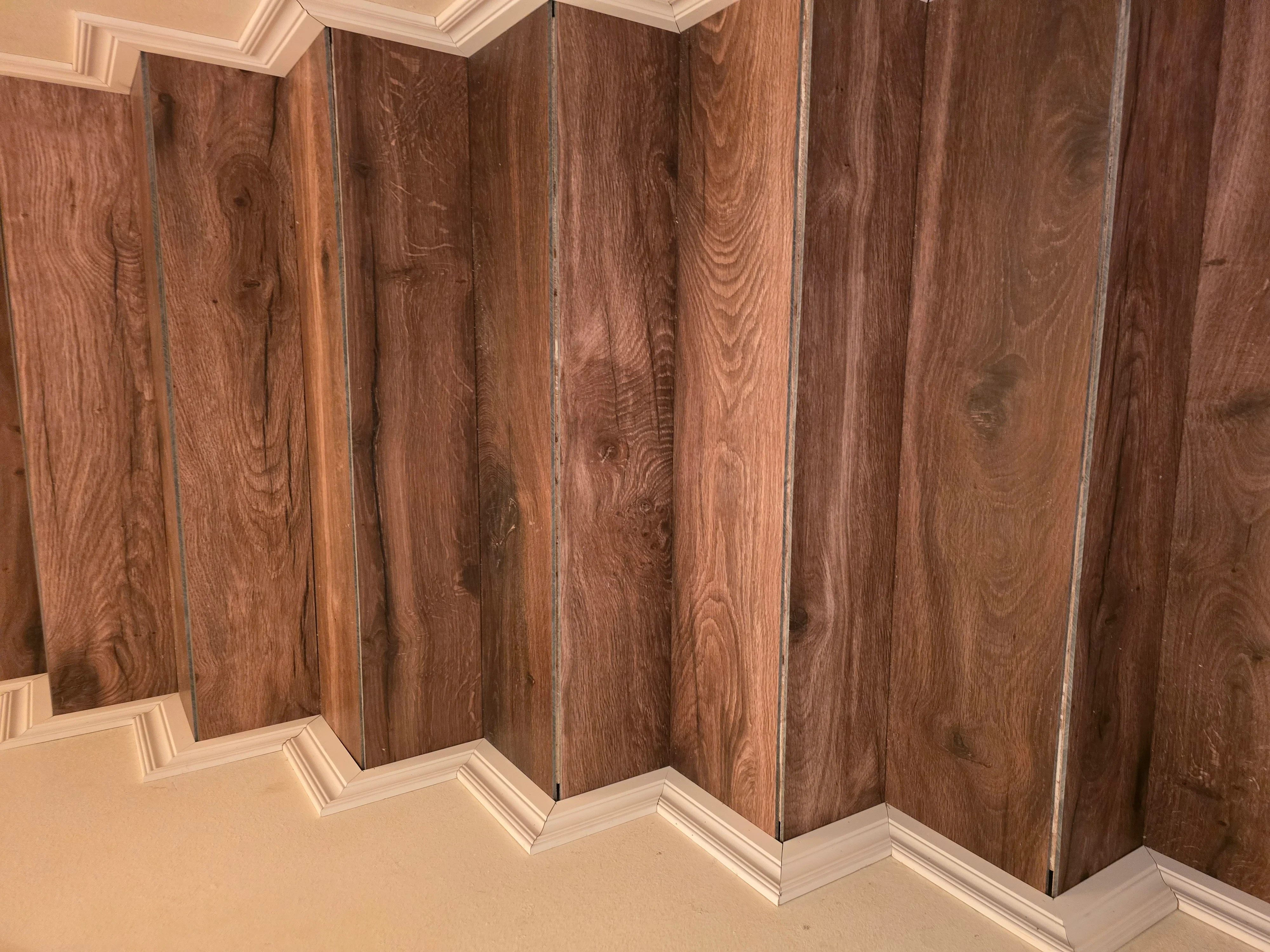 Medium-brown hardwood flooring with white trim and crown molding in corner installation